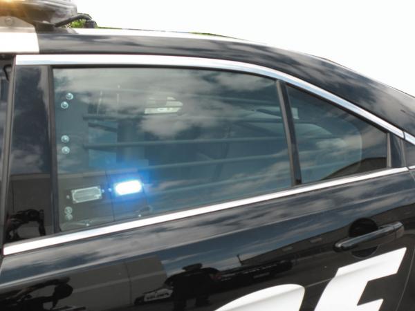 D&R 937-0320A rear window bar inside the back door of a black-and-white police sedan, blue LED lit