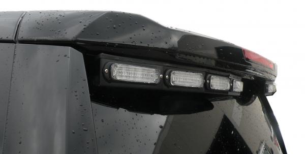 Close-up of the unlit clear lenses in their black bracket under the spoiler edge of a Chevy Tahoe
