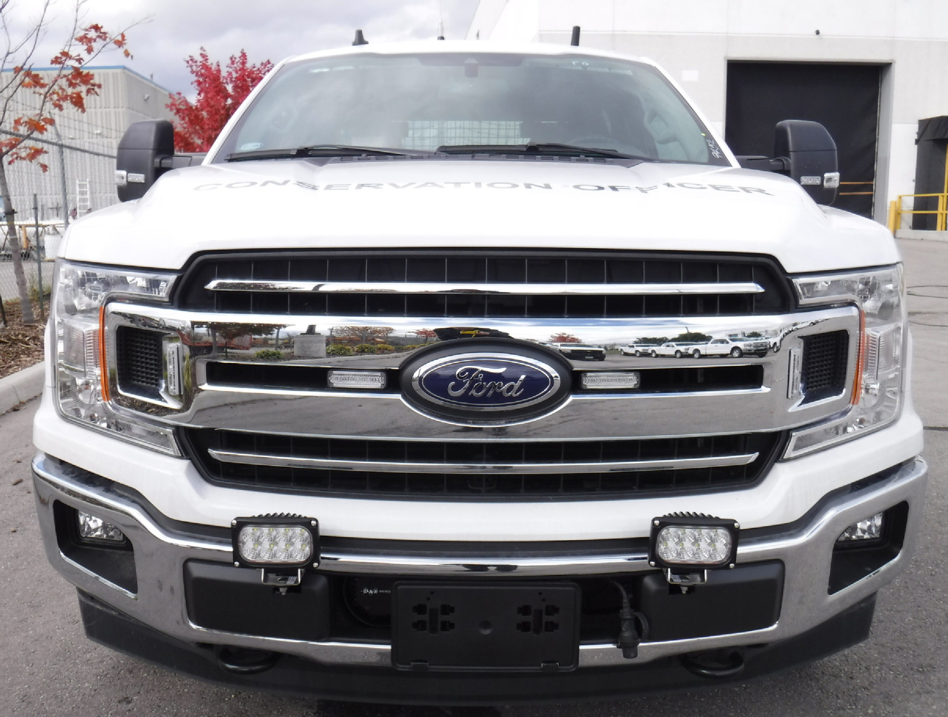 Two of the lamps mounted low on the front bumper of a white Ford pickup lettered CONSERVATION OFFICER